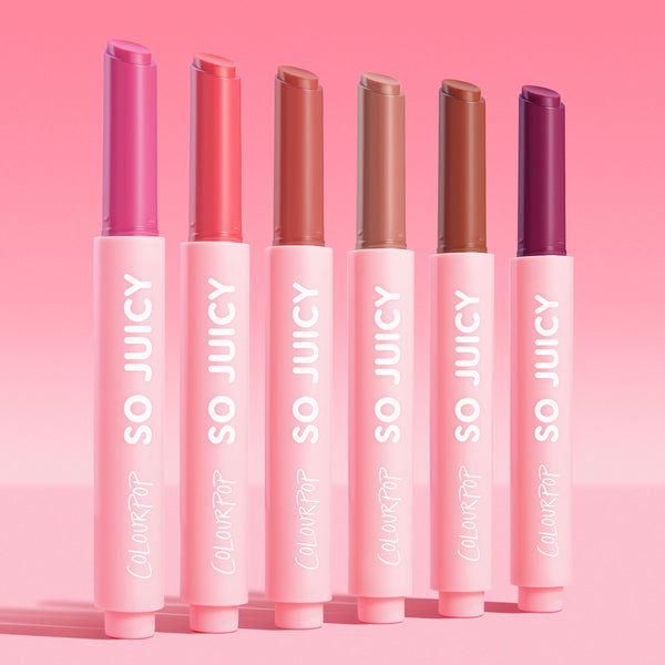 Six ColourPop So Juicy Plumping Gloss Balm with Peptides sticks stand upright, caps off to reveal pink, coral, nude, caramel, terracotta, and deep berry shades in matte pink tubes labeled SO JUICY, lined on a pink gradient background - So Balm bundle.