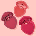Three heart-shaped blush compacts open to reveal matte pans in coral, rose, and fuchsia, arranged diagonally on a pale pink background; Heart to Heart ColourPop Heart Powder Blush Set for buildable cheek color.