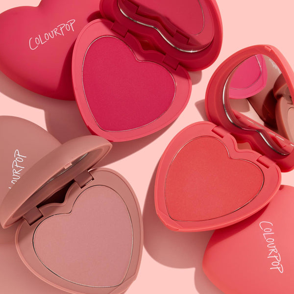 Totally Lovestruck ColourPop Heart Powder Blush Set features heart-shaped compacts opened to show hot pink, coral, and soft mauve powders with built-in mirrors and ColourPop logos, arranged on a blush-pink background.