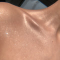 Shimmering collarbone skin glistens as Sterling Silver ColourPop SOL Shimmering Dry Oil catches the sun, showcasing fine micro-sparkle and a luminous glow across the shoulder and neck in a tight, sunlit close-up.