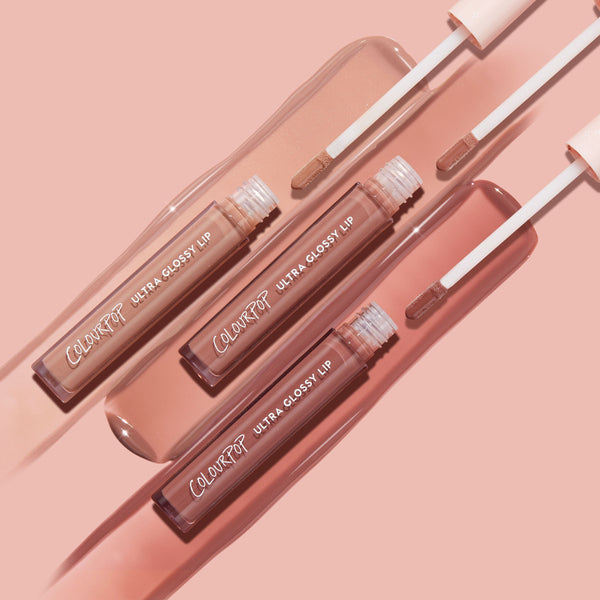ColourPop Ultra Glossy Lip Cool Nudes trio, open tubes with doe-foot applicators swiping beige, rose, and mauve nude gloss swatches on a blush-pink backdrop, highlighting the high-shine finish.