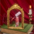 Beautiful Belle Disney Princess lip mask and ultra glossy lip gloss with applicator wand resting in an open pink tube, framed by an ornate gold mirror on stacked books with a red rose and candle in a romantic fairytale setting.