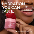 Strawberry Milk ColourPop Lip Scrub jar topped with a fresh strawberry, held beside glossy smiling lips; pink frosted pot reads “Strawberry Milk Lip Scrub,” highlighting the strawberry milk flavor in a close-up beauty product shot.