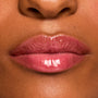 Glossy pink lips wearing a shade from the Fruit Basket ColourPop Glossy Lip Balm Trio, showing a sheer tint and high-shine, hydrated finish in a tight macro close-up on medium-brown skin.