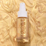 Clear glass bottle of ColourPop SOL Glow Oil, It’s a Wolf Thing, standing upright with a white pump and gold SOL logo, showcasing shimmering golden body oil against a swirled metallic gold backdrop.