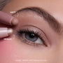 Close-up of a fair-skinned model’s blue eye wearing shimmery neutral shadow created with the All Eyes On Me Heart to Get Shadow Stix Set, showing matte and metallic cream eyeshadow tips applying blendable color on the eyelid.