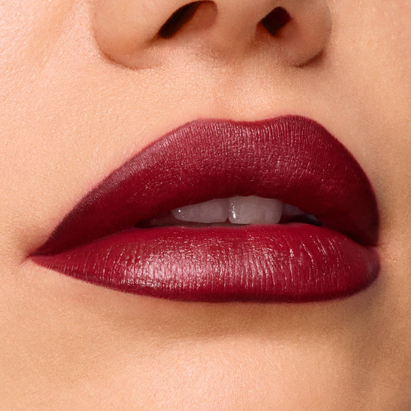 Slow Burn ColourPop Lux Lipstick draping full lips in a deep wine‑burgundy satin finish, showing smooth, precise edges and creamy payoff in a tight macro beauty close‑up.