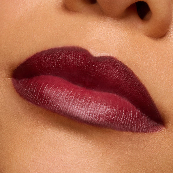 Lips wearing Slow Burn, a deep burgundy ColourPop Lux Lipstick, showing smooth full-coverage satin-matte color with crisp edges in a macro studio close-up, highlighting rich pigment and creamy texture.