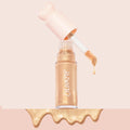 ColourPop Liquid Highlighter in Sugar Donut drips from a doe-foot applicator, a golden shimmer drop beside the clear tube with a pink heart-shaped cap, set on a soft blush backdrop with a glossy metallic swatch pooling at the bottom.