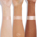 Special Guest swatched in thick stripes on three wrists with light, medium, and deep skin tones, showing a champagne-pearl, high-shine finish of the ColourPop Super Shock Highlighter on a clean white background with a small ColourPop heart logo.
