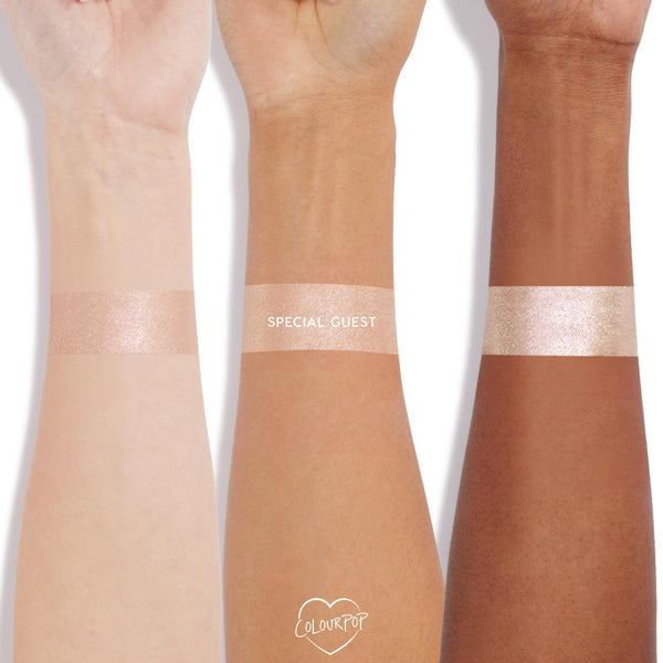 Special Guest swatched in thick stripes on three wrists with light, medium, and deep skin tones, showing a champagne-pearl, high-shine finish of the ColourPop Super Shock Highlighter on a clean white background with a small ColourPop heart logo.