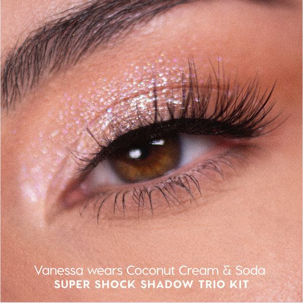 Close-up of a brown eye wearing Sweet Sips Super Shock Shadow in shimmering Coconut Cream & Soda, showing glittery champagne-pink lid color and long voluminous lashes, promoting the full collection set trio kit makeup look.