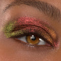 Shimmering multichrome eyeshadow illuminates a hazel eye, with red-rose, copper, and lime-green shifts swept across the lid using ColourPop Shadow Stix in Love Triangle, showcasing bold pigment and a metallic finish in a close-up.