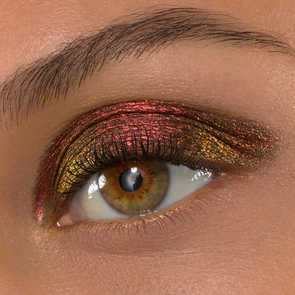 Vampire Girl ColourPop Shadow Stix sweeps across a hazel eye, creating a metallic multichrome look that shifts from ruby red to antique gold on the upper lid, framed by defined lashes and a natural brow in a macro beauty shot.