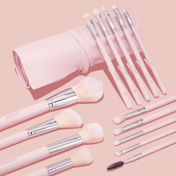 Smoke 'N Roses Brush Roll showcasing a ColourPop Makeup Brush Kit: pink-handled face and eye brushes with soft blush bristles and silver ferrules, plus spoolie and angled liner, fanned from a blush roll embossed ColourPop on a pastel pink background.