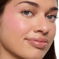 Crowd Favorite ColourPop Cream Blush melts into skin, giving a soft pink, dewy flush on a model’s cheek; close-up face shows blended pigment with natural glow, long lashes, and glossy lips against a white background.