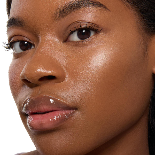 ColourPop Super Shock Highlighter in Ohana catching light on the cheekbone, delivering a luminous champagne glow on dewy skin with natural lashes and glossy lips in a close-up beauty shot.