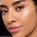 Model wearing Ohana Super Shock Highlighter, showing a luminous champagne glow on the cheekbone with defined brows and glossy lips in a tight face crop; part of the Disney Lilo & Stitch Collection, ColourPop Full Collection Set.