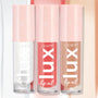 Three ColourPop Lux Lip Oil tubes stand side by side in the Top Hits bundle, displaying clear, coral pink, and warm nude shades with pink star-print caps against a soft pastel backdrop.