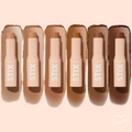 ColourPop Bronzer Stix in Laguna Beach shown upright and uncapped in a lineup of six bronze shades, each stick with a matching swipe behind it on a soft peach background, highlighting the creamy twist-up bronzer packaging.
