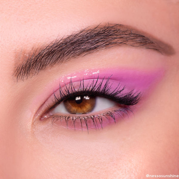 Brown eye wears In The Clear Face & Eye Gloss, creating a glassy wet-look over pink‑lavender shadow; fluttery lashes and a defined brow frame the lid, showcasing ColourPop Face & Eye Gloss shine in a macro beauty close-up.