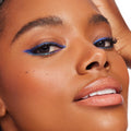 Ventura Blvd ColourPop Chrome Crème Gel Liner sweeping a bold cobalt-blue wing with a teal duochrome shift along upper and lower lash lines, shown in a close-up on a model with smooth skin and glossy nude lips against a bright studio backdrop.