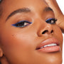 Ventura Blvd ColourPop Chrome Crème Gel Liner sweeping a bold cobalt-blue wing with a teal duochrome shift along upper and lower lash lines, shown in a close-up on a model with smooth skin and glossy nude lips against a bright studio backdrop.