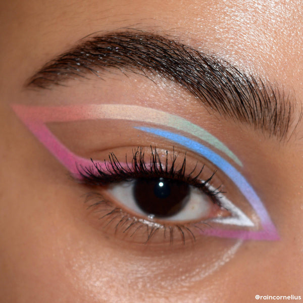 Pastel graphic eyeliner sweeps across a model’s eyelid - pink, beige, mint, blue, lavender, and white - showcasing Sweet Fantasy, a ColourPop Shadow Palette & Brush Set, with crisp lines and soft shimmer in a clean close-up beauty shot.