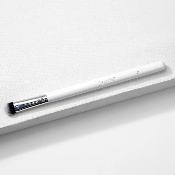 ColourPop Medium Dome Brush blending detail eye makeup - white-handled makeup brush with chrome ferrule and domed black‑to‑white bristles, marked E7 - resting diagonally on a minimalist white textured backdrop.