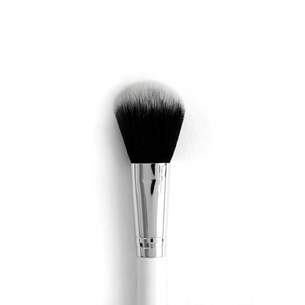 Blush brush with tapered, fluffy black-to-white synthetic bristles blending powder across cheeks, anchored by a chrome ferrule and white handle on a clean white background; ColourPop Makeup Brush for precise, soft application.