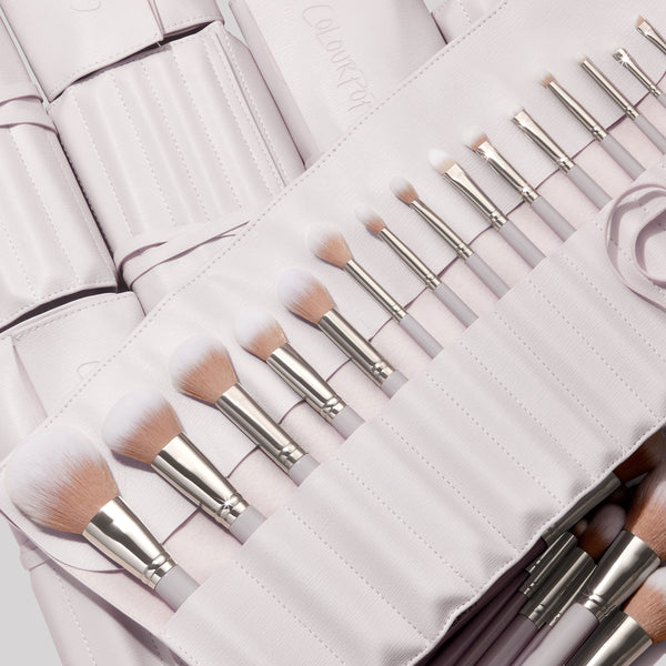The Ultimate Stunner, a ColourPop Shadow Palette & Brush Set, displays white-tipped face and eye brushes with silver ferrules neatly lined in a pale stone faux-leather roll case, pastel handles visible and ready for precise application.