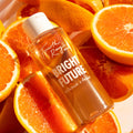ColourPop Fourth Ray Beauty Bright Future Vitamin C Tonic bottle tilted among juicy orange halves, amber formula glowing in warm light with a white cap and bold BRIGHT FUTURE label, emphasizing citrus-powered Vitamin C tonic skincare.