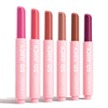 Six ColourPop So Juicy Plumping Gloss Balm with Peptides sticks, So Balm, stand upright and uncapped on a white background, displaying fuchsia, coral, rosy nude, beige, warm brown, and deep berry in pink tubes labeled SO JUICY.