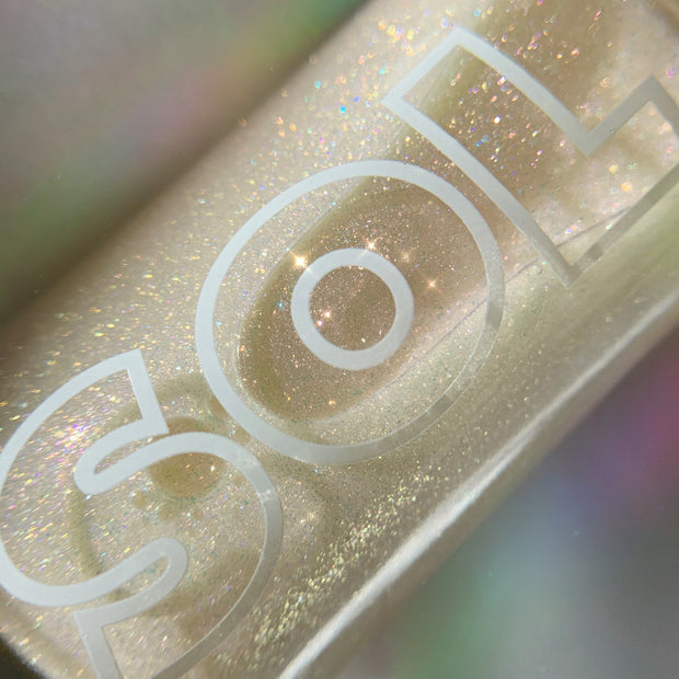 SOL-labeled bottle sparkles as fine rainbow glitter swirls in a golden base; ColourPop SOL Shimmering Dry Oil, Rainbow Glow, shown in a tight macro against a soft iridescent backdrop for a luminous body sheen.