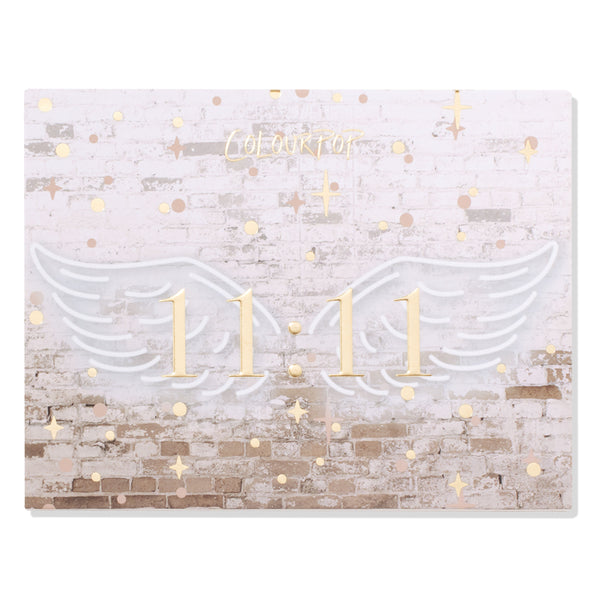 11:11 ColourPop Shadow Palette closed, featuring gold 11:11 centered between white angel wings on a faded white brick backdrop with scattered gold stars and dots, ColourPop logo above - front cover of the eyeshadow palette.