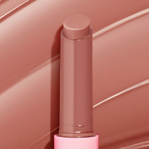 ColourPop So Juicy Plumping Gloss Balm with Peptides in Doe stands uncapped, twist-up stick revealing a creamy warm nude-brown tint, set against matching glossy swipes, in a pink tube for a plumping, glossy finish.