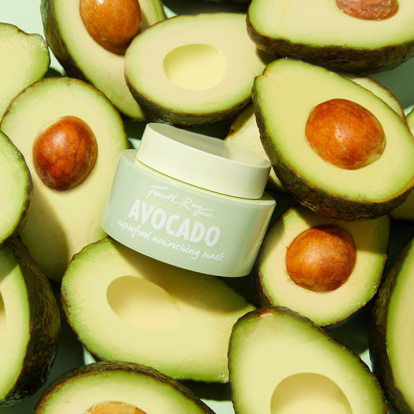 Fourth Ray Beauty Avocado Superfood Mask face mask jar resting among ripe avocado halves on a mint-green backdrop, pale green container with white lid showcasing a hydrating ColourPop Face Mask for nourishing skin.