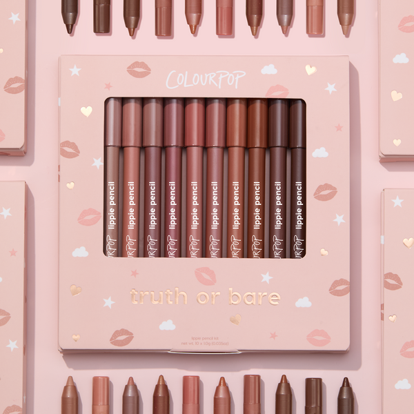 Truth or Bare Lippie Pencil kit by ColourPop displayed in a pink windowed box, 10 nude lip liner shades from peach to deep brown standing upright, surrounded by matching pencils and boxes on a pastel pink background with kiss and star icons.