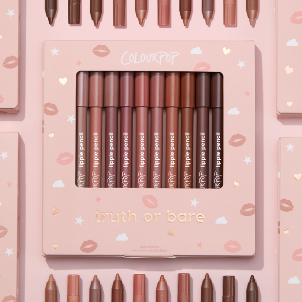 Truth or Bare Lippie Pencil kit by ColourPop displayed in a pink windowed box, 10 nude lip liner shades from peach to deep brown standing upright, surrounded by matching pencils and boxes on a pastel pink background with kiss and star icons.