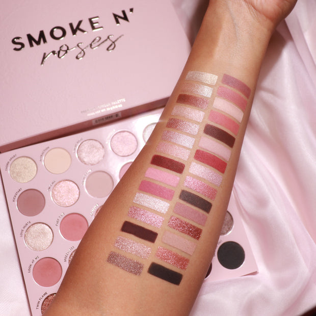 ColourPop Smoke 'N Roses shadow palette swatched on an arm, displaying rosy pinks, mauves, taupes, silvers, and deep browns in matte and shimmer finishes beside the open ColourPop Shadow Palette on a soft pink satin background.