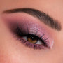Shimmery mauve-pink eyeshadow blends into deep plum on a brown eye, finished with fluttery lashes, showcasing Rock Candy shades from the ColourPop Shadow Palette in a close-up beauty look for soft glam.