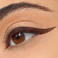 Winged eyeliner defines the upper lash line in a sharp, deep-brown cat eye, created with ColourPop BFF Liquid Liner in Grande, on a close-up of a brown eye with soft nude shadow and a groomed brow.