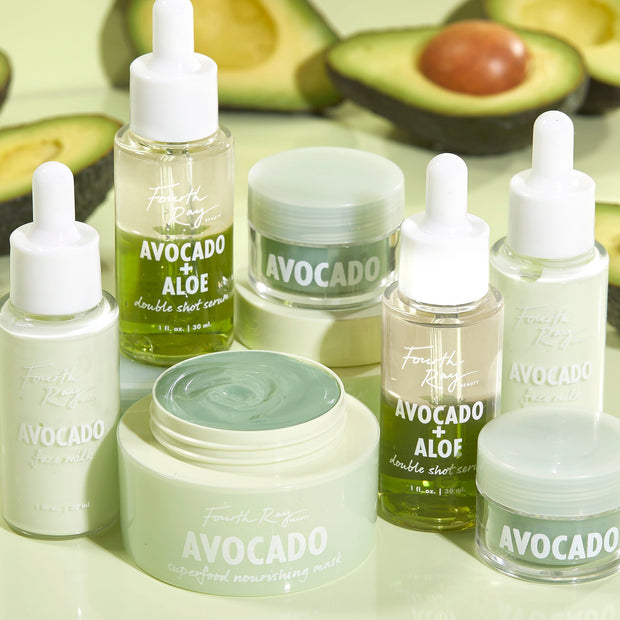Avocado Superfood Mask by Fourth Ray Beauty sits open with a swirl of pale-green cream, presented as a ColourPop Face Mask, surrounded by Avocado + Aloe double shot serum bottles, face milks, and jars on a mint backdrop with halved avocados.