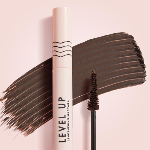 ColourPop Level Up Brown lengthening mascara, tube and tapered spoolie sweeping a rich brown swatch across a soft pink background, showcasing the deep pigment and brush detail for this Brown shade.