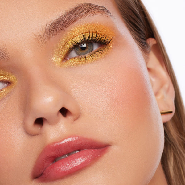 Shimmering golden-yellow eye makeup showcases Montecito Super Shock Shadow by ColourPop, swept across the lids and inner corners with bold sparkle and defined lashes, in a close-up beauty shot highlighting smooth, dewy skin.