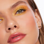 Shimmering golden-yellow eye makeup showcases Montecito Super Shock Shadow by ColourPop, swept across the lids and inner corners with bold sparkle and defined lashes, in a close-up beauty shot highlighting smooth, dewy skin.