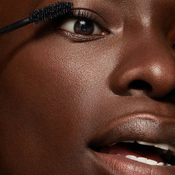 ColourPop Act Natural Mascara in Black brushing through upper eyelashes with a tapered bristle wand, close-up on a model’s eye for defined, natural-looking length and lift.