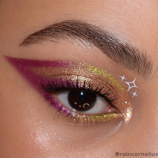 Green Juice ColourPop Super Shock Shadow sweeps a lime‑gold shimmer across the eyelid, paired with a bold magenta wing, glittered lower lash line, and white star decals in a close‑up eye look showcasing metallic payoff and sparkle.