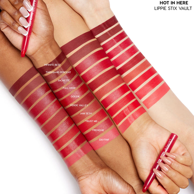 ColourPop Heat Warning Lippie Vault Set shows swatches across three forearms, featuring ten Lippie Stix red tones from deep burgundy to bright coral - Infinite Best, Bichette, Goldie, Trust Me, Frenchie, Daytrip - on a white background.