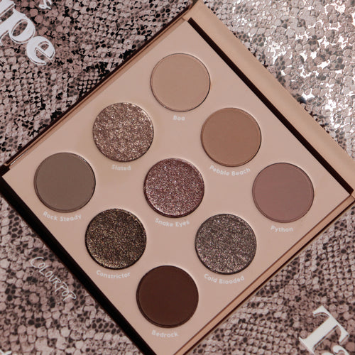 ColourPop Shadow Palette “That’s Taupe” open to nine cool‑toned taupe neutrals - mattes and metallic shimmers like Rock Steady, Slated, Snake Eyes, and Bedrock - arranged 3x3 on a beige tray atop a snakeskin-patterned background.